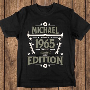 Puede incluir: Camiseta negra con un diseño vintage. El diseño incluye el nombre "MICHAEL", el año "1965" y las palabras "LIMITED EDITION". El diseño también presenta herramientas y engranajes en blanco y gris.
