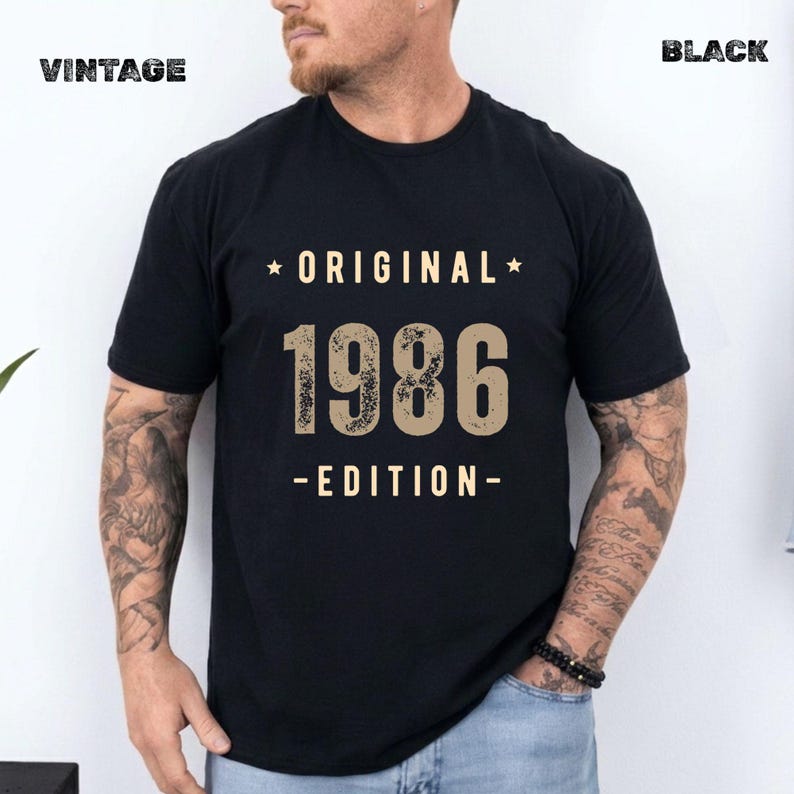 May include: A black short-sleeved t-shirt featuring the text "ORIGINAL 1986 EDITION" in a distressed beige font. The word "ORIGINAL" is centred above the large numbers "1986," with "EDITION" below, all flanked by small stars.