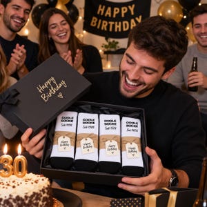 May include: A black gift box containing four pairs of white socks with black toes and heels. Each pair features the text "COOLE SOCKE" and a specific year, including 1996, 1986, 1976, and 2005. Each pair has a brown paper band with a "Happy Birthday" tag.