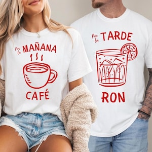 Puede incluir: Dos camisetas blancas con estampados gráficos en rojo. La camiseta de la izquierda presenta un icono de taza de café con el texto Por la MAÑANA CAFÉ. La de la derecha muestra un vaso con hielo y una rodaja de cítrico con el texto Por la TARDE RON.