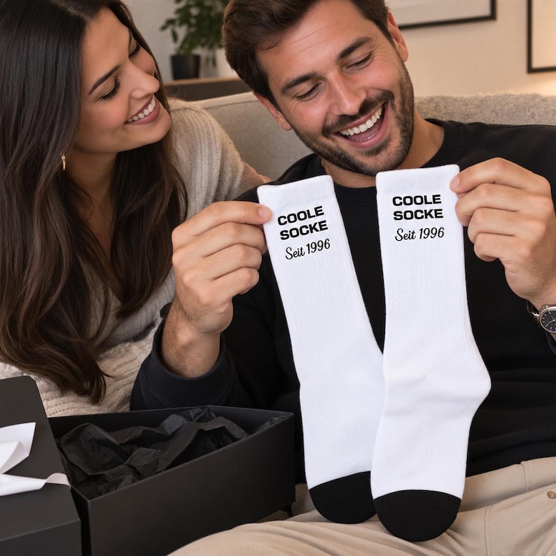 May include: A pair of white crew socks with black heels and toes. The text COOLE SOCKE is printed in a bold black sans-serif font, followed by the text Seit 1996 in a black serif font on the upper portion of each sock.
