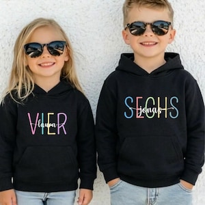 May include: A white ceramic mug with a black handle and the text "But First, Coffee" in a bold, black font. The mug is set against a blurred background, suggesting a cozy setting. The mug appears to be approximately 4 inches tall.