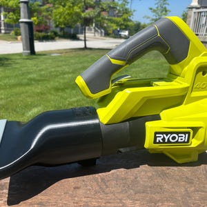 May include: A lime green and grey cordless leaf blower with a black nozzle. The blower has a handle with a grey grip and the brand name "RYOBI" is visible on the side. The blower is labelled "40V".