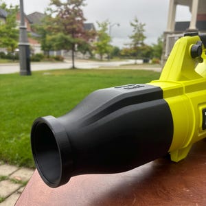 May include: A yellow and black leaf blower with a black nozzle. The blower is sitting on a wooden surface.