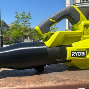 May include: A cordless RYOBI 40V leaf blower. It has a black nozzle and body, with a yellow and grey handle and housing. The RYOBI logo is visible. Designed for outdoor use, it is suitable for clearing leaves and debris.