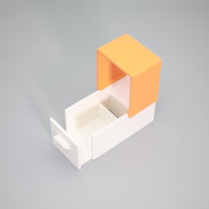 K&ouml;nnte beinhalten: Zweifarbige Aufbewahrungsbox mit offener Schublade. Der obere Teil ist leuchtend orange, im Kontrast zu der wei&szlig;en Schublade und dem Sockel. Die Schublade ist teilweise herausgezogen und zeigt ein Innenfach. Minimalistisches und geometrisches Design.