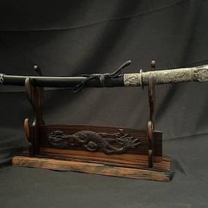 以下が含まれることがあります： 黒い鞘と、龍の頭のデザインが施された銀色の柄が付いた装飾用の剣。剣は、龍のモチーフが彫られた木製のスタンドに置かれています。スタンドは濃い茶色の木材で作られています。