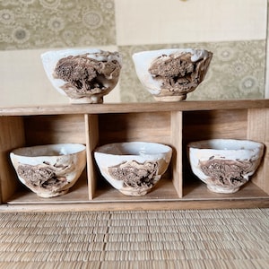 以下が含まれることがあります： 茶碗5個セット。白地に茶色の釉薬がかかった、独特の質感の茶碗。木製の箱に入っています。