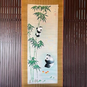以下が含まれることがあります： 竹林の中にいる白黒のパンダ2匹を描いた、伝統的な中国の巻物絵画。パンダは写実的なスタイルで描かれており、竹は様式化された方法で描かれている。巻物は木製の棒に巻き付けられており、金色の縁取りが施されている。