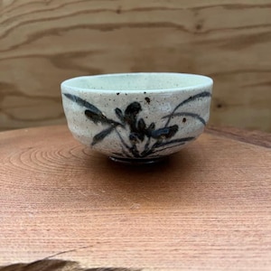 以下が含まれることがあります： テクスチャ加工された表面を持つ、小さなオフホワイトのセラミックボウル。 ボウルは、暗い抽象的な花の模様が特徴です。 ボウルは木製の表面に置かれています。