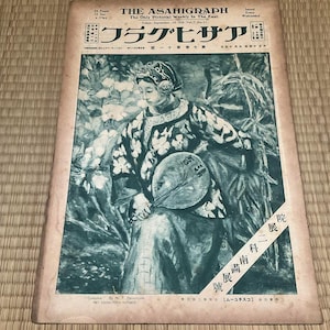 以下が含まれることがあります： 「The Asahigraph」のヴィンテージ日本の雑誌の表紙。伝統的な衣装を着て扇子を持つ女性の水彩イラストが特徴です。表紙には日本語のテキストがあり、1926年9月15日の日付が入っています。雑誌は織りマットの上にあります。