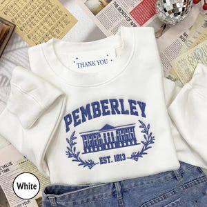 May include: White crewneck sweatshirt with a blue embroidered design of a building with the text "PEMBERLEY EST. 1813" and the words "THANK YOU" on a white tag.