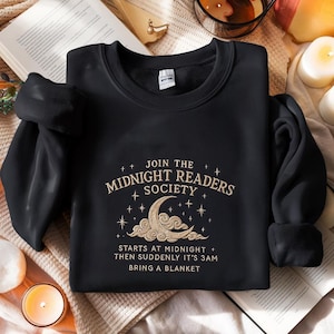 May include: Black sweatshirt with a gold embroidered design that says "Join the Midnight Readers Society" with a crescent moon and stars. The text below says "Starts at midnight + then suddenly it's 3am. Bring a blanket."