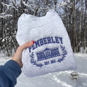May include: A gray sweatshirt with a blue embroidered design that says "Pemberley Est. 1813". The design features a building with a wreath around it.