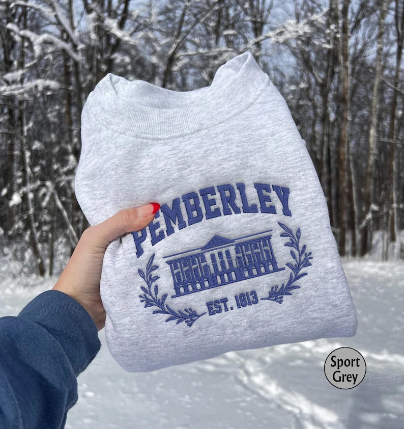 May include: A gray sweatshirt with a blue embroidered design that says "Pemberley Est. 1813". The design features a building with a wreath around it.