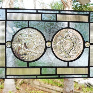 May include: A rectangular stained glass panel featuring two central circular clear glass inserts with a starburst pattern. The panel is framed with black lead cames and includes textured clear glass segments, ribbed glass borders, and small clear glass spheres.
