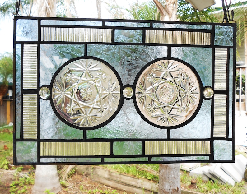 May include: A rectangular stained glass panel featuring two central circular clear glass inserts with a starburst pattern. The panel is framed with black lead cames and includes textured clear glass segments, ribbed glass borders, and small clear glass spheres.