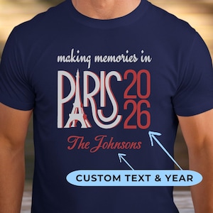 May include: A navy blue short-sleeve t-shirt featuring the white text "making memories in" above a large graphic of the Eiffel Tower integrated into the word "PARIS" in white and red, with "2026" and "The Johnsons" printed in red below.
