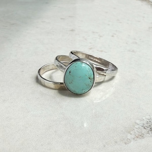 May include: Three silver rings. One ring features a large, oval turquoise stone. The other two rings are simple bands with a hammered texture. The rings are displayed on a white surface.