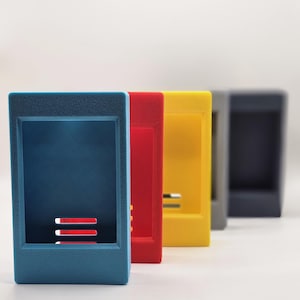 May include: A row of five rectangular, open-faced plastic storage containers arranged in a line. The containers are coloured blue, red, yellow, light grey, and dark grey, each featuring a hollow centre and three horizontal ventilation slots.