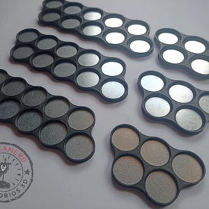 May include: Five different sized black plastic paint pot holders with circular indentations. The holders are designed to hold round paint pots. The holders are on a white surface.