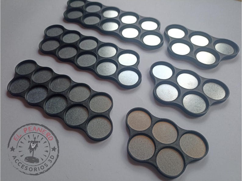 May include: Five different sized black plastic paint pot holders with circular indentations. The holders are designed to hold round paint pots. The holders are on a white surface.
