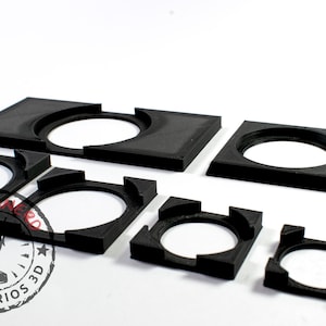 Puede incluir: Un conjunto de seis anillos de plástico negro de diferentes tamaños. Los anillos están diseñados para sujetar objetos en su lugar, como lentes de cámara u otros objetos circulares.