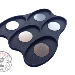 May include: Black plastic tray with six oval-shaped compartments. Each compartment has a round, metallic disc inside. The tray has a logo on the bottom that says "El Peanero Accesorios 3D".