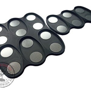 May include: Two black plastic trays with circular indentations for holding small items. The trays are designed to hold paint pots or other small containers.