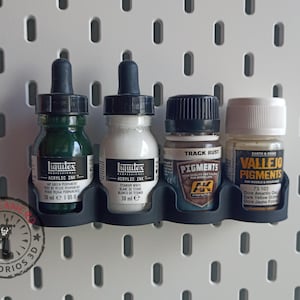 May include: Four bottles of acrylic ink and paint in a black plastic holder. The bottles are labelled Liquitex Acrylic Ink, Liquitex Acrylic Ink, Track Rust Pigments, and Vallejo Pigments. The bottles are 30 ml each.