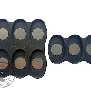 May include: Two black plastic trays with circular indentations for holding small round objects. The larger tray has six indentations and the smaller tray has three indentations.