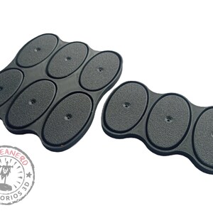 May include: Two sets of black oval-shaped bases for miniature figures. The larger set has six bases, while the smaller set has three bases. The bases are made of a textured material and have a small hole in the center of each base.
