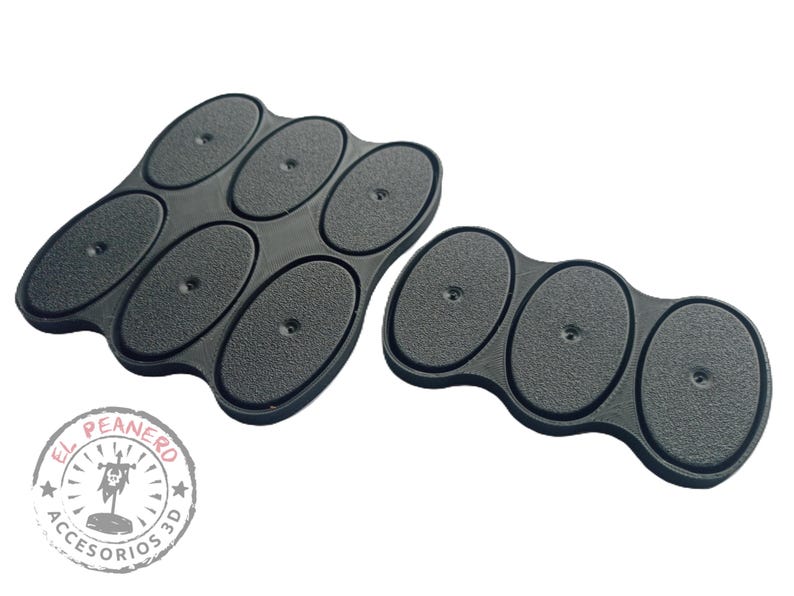 May include: Two sets of black oval-shaped bases for miniature figures. The larger set has six bases, while the smaller set has three bases. The bases are made of a textured material and have a small hole in the center of each base.
