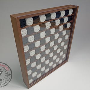 May include: A wooden frame with a clear glass front displays a checkerboard pattern of black and white counters. The counters are arranged in a grid pattern.