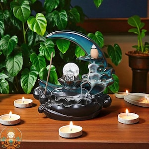 May include: A ceramic incense burner shaped like a crescent moon, with a blue and black glaze. It has a crystal ball, a lotus flower base, and a small incense cone. Tea light candles surround the burner on a wooden surface.