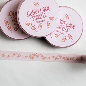 May include: Pink washi tape with a repeating pattern of candy corn. The tape is rolled up and the label reads "Candy Corn Sparkles Washi".