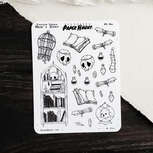 May include: A white sticker sheet titled Paper Haunt Mage's Study featuring black line art illustrations of a birdcage, skulls, open books, scrolls, potion bottles, crystals, a candle, and a tall arched bookshelf filled with various books.