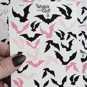 Pode incluir: Uma folha de adesivos com morcegos pretos e rosa. Os adesivos estão dispostos em um padrão repetitivo sobre um fundo branco. A folha é etiquetada como "Bats" e "Vampire's Crypt".