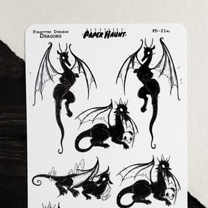 May include: A white sticker sheet titled Forgotten Dungeon Dragons by Paper Haunt, featuring seven black ink illustrations of dragons in various poses, some holding skulls or near crystals, with the code FD-21BL and the website paperhaunt.com.