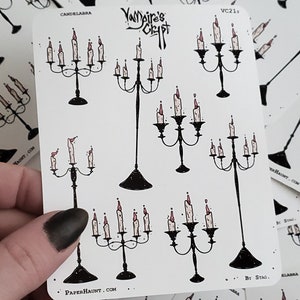 Puede incluir: Una hoja de pegatinas con varias ilustraciones en blanco y negro de candelabros con velas rojas. Las pegatinas están etiquetadas con "Vampire's Crypt" y "PaperHaunt.com".