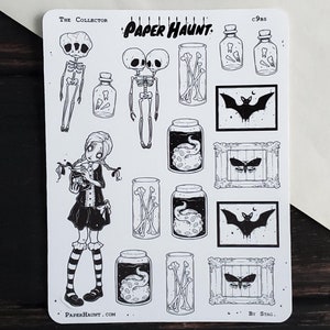 May include: A sheet of black and white stickers featuring a spooky theme. The stickers include a girl holding a jar, skeletons, bats, jars with bones, and frames with moths. The text "Paper Haunt" is at the top of the sheet.