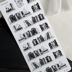 May include: A sheet of black and white stickers featuring illustrations of bookshelves with books, skulls, and candles. The text "Book Shelves" and "The Haunted Library" are visible on the sheet.