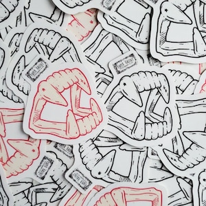 May include: A collection of black and white stickers featuring a stylized illustration of a set of fangs. Some of the stickers have a red and white color scheme.