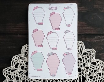 May include: A sheet of coffin-shaped note page stickers. The stickers are pink, white, and light blue with a pink, white, and gray border. The stickers have a dotted line down the center and a small coffin with a cross on top at the bottom of each sticker. The text "COFFIN. NOTE PAGE STICKERS" is at the top of the sheet.