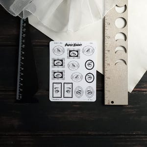 May include: A sheet of stickers featuring various black and white illustrations of eyes in frames. The stickers are labeled "PAPER HAUNT" and "Lover's Eye".