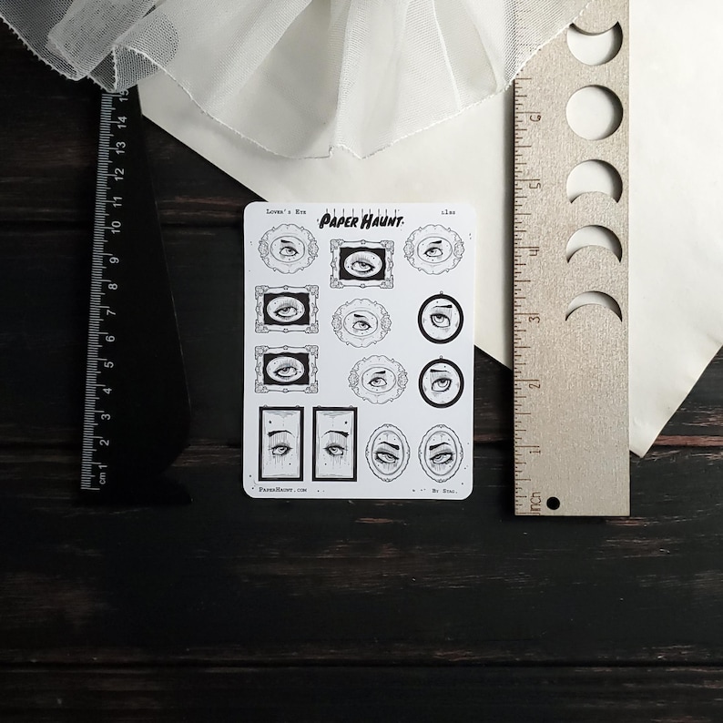 May include: A sheet of stickers featuring various black and white illustrations of eyes in frames. The stickers are labeled "PAPER HAUNT" and "Lover's Eye".