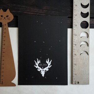 Puede incluir: Impresi&oacute;n en blanco y negro de una calavera de ciervo con cuernos sobre un fondo negro con estrellas blancas. La impresi&oacute;n tiene el texto "Paper Haircut" y "Dystopia" en blanco.