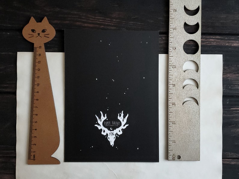 Puede incluir: Impresi&oacute;n en blanco y negro de una calavera de ciervo con cuernos sobre un fondo negro con estrellas blancas. La impresi&oacute;n tiene el texto "Paper Haircut" y "Dystopia" en blanco.