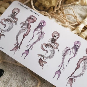 May include: Five illustrations of skeletal mermaids with purple and white colouring. The mermaids are drawn in a whimsical style with flowing hair and tails. The text "Fishbones - Mermaids" is at the top of the image.