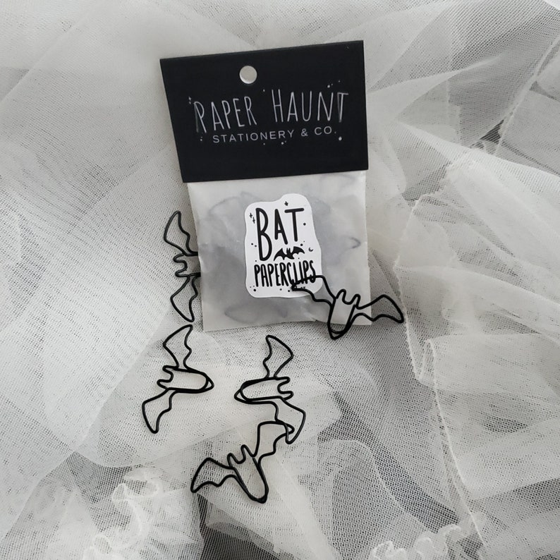 May include: A package of black metal bat-shaped paperclips. The package is labeled "Paper Haunt Stationery & Co." and "Bat Paperclips".